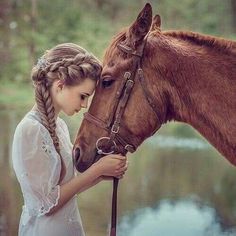 a woman is petting the head of a brown horse in front of a body of water