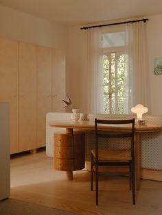 a room with a table, chair and cabinet next to a window that has curtains on it