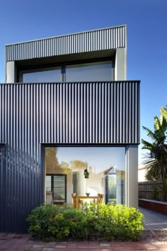 a modern house with large windows and metal sidings on the outside, surrounded by greenery