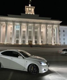 a white car parked in front of a large building with columns on it's sides