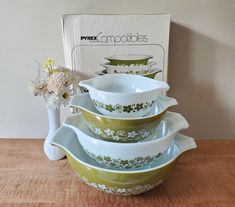 three bowls stacked on top of each other with flowers in the middle and a box behind them