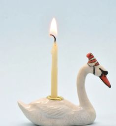 a white swan with a red and black hat on it's head is next to a lit candle