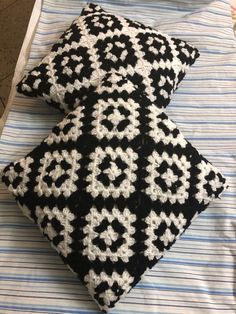 two black and white crocheted pillows sitting on top of a blue striped blanket