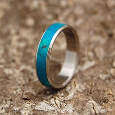 a turquoise ring with silver inlays sits on a rock