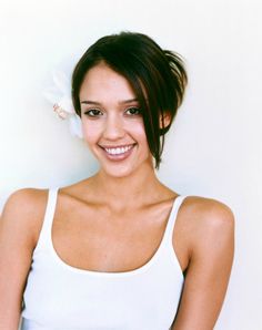 a beautiful young woman with a flower in her hair smiling at the camera while wearing a white tank top