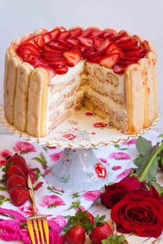 a cake with strawberries on top is cut in half and sits on a floral tablecloth