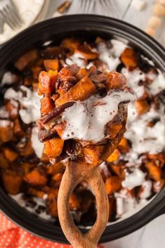 a wooden spoon holding up a scoopful of sweet potato casserole with sour cream on top