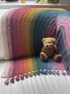 a crocheted blanket with a teddy bear sitting on the couch next to it