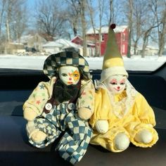 two stuffed clowns sitting in the back seat of a car on a snowy day