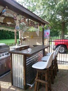 an outdoor bar with two stools next to it and a grill in the background