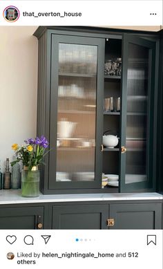 a green cabinet with glass doors and flowers in vases on the counter top next to it