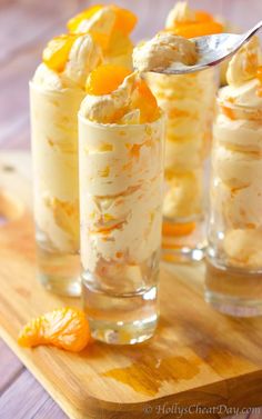 three glasses filled with dessert sitting on top of a cutting board next to an orange slice