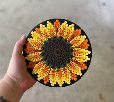 a hand holding a small colorful object in the shape of a sunflower with dots on it