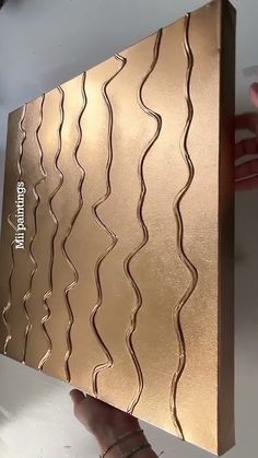 a person is holding up a piece of art that looks like wavy lines on gold foil