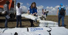 several people unloading bags from a truck in an open field with blue sky and clouds behind them