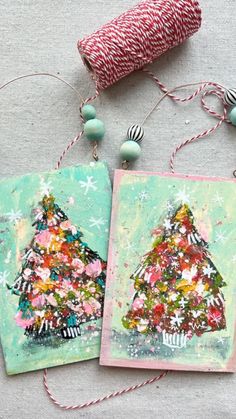 two christmas cards on a table with twine and spools of thread next to them