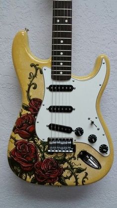 an electric guitar with roses painted on it's body is hanging from the wall