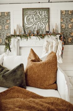 a white couch with pillows and blankets on it in front of a christmas fireplace mantel