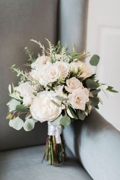 a bouquet of white flowers sitting on top of a gray couch next to a window