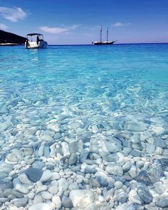 two boats floating on top of a body of water next to rocks and pebbles in the ocean