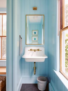 a bathroom sink sitting under a mirror next to a window in a blue painted room