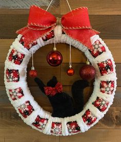 a christmas wreath hanging on the wall with ornaments around it and a black cat wearing a red bow