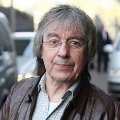 an older man with glasses and a leather jacket is standing in front of some cars