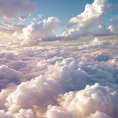 the view from an airplane window shows clouds and blue sky in the foreground, as well as white fluffy clouds