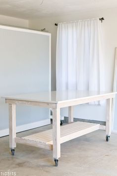 a white table with wheels on it in front of a curtained wall and floor