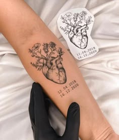 a heart tattoo on the arm with flowers and plants in it, next to a glove