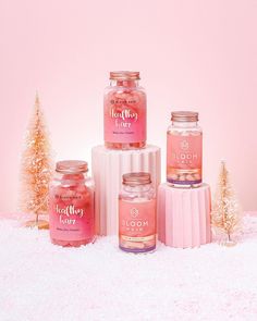 three jars with pink liquid sitting on top of snow covered ground next to small trees