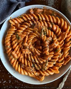 a white bowl filled with pasta covered in sauce and seasoning on top of a wooden table