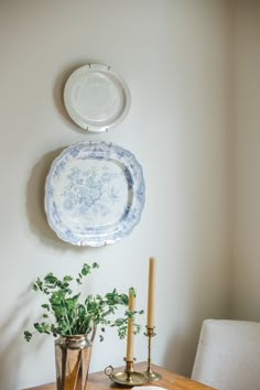 a dining room table with two plates on the wall above it and a plant in a vase