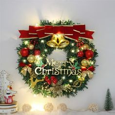 a christmas wreath on the wall with lights and decorations around it, next to a small tree