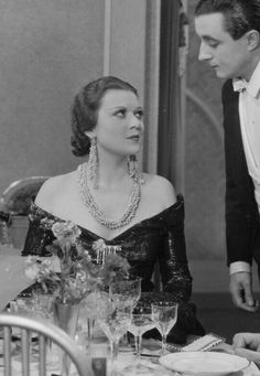 an old black and white photo of a man standing next to a woman at a dinner table