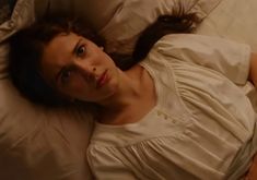 a woman laying on top of a bed in a white shirt and tan pillow cover