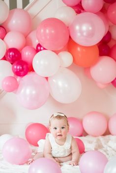 a baby sitting on a bed surrounded by pink and white balloons