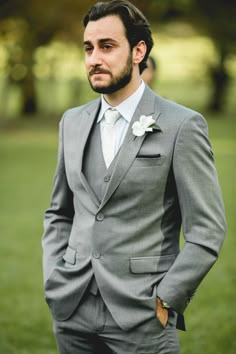 a man in a gray suit and white flower boutonniere is posing for the camera