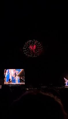 fireworks are lit up in the night sky above people watching televisions on their cell phones