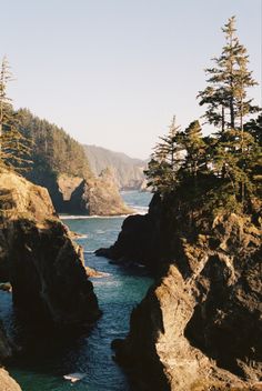 the water is blue and green with rocks on both sides that are surrounded by pine trees