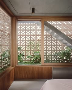 a bed sitting under a window next to a wooden wall with lattice design on it