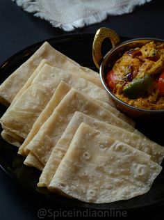 some pita bread on a black plate with a small bowl of curry next to it