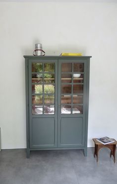 a gray cabinet with glass doors in a living room next to a small side table