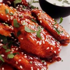 a white plate topped with chicken wings covered in sesame seeds and garnishes