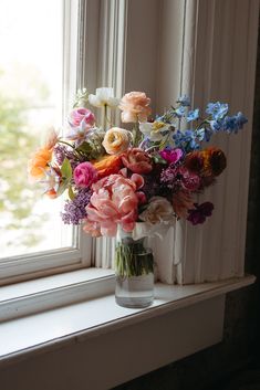 a vase filled with lots of colorful flowers on top of a window sill next to a window