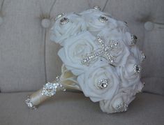 a bridal bouquet with white roses and crystal cross brooches sits on a couch