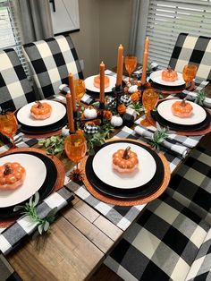 a dining room table set with black and white place settings, pumpkins on the plates