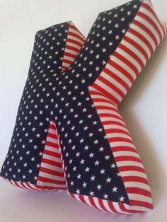 a red, white and blue pillow with an x on it's side that is made out of american flag fabric