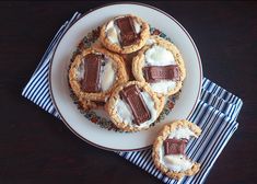 four cookies with marshmallows and chocolate on a white plate next to a blue striped napkin