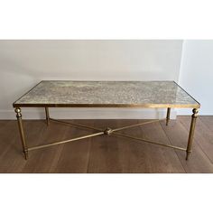 a marble top coffee table with brass legs on a wooden floor in front of a white wall